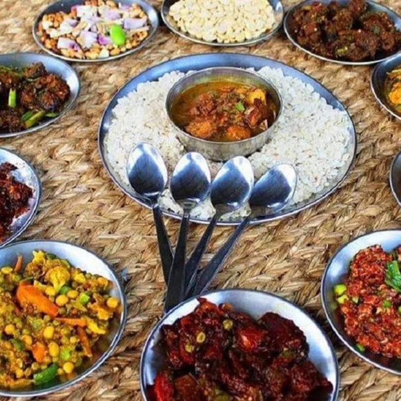 A variety of Nepalese dishes, including rice, curry, and vegetables, served in metal bowls on a woven mat.